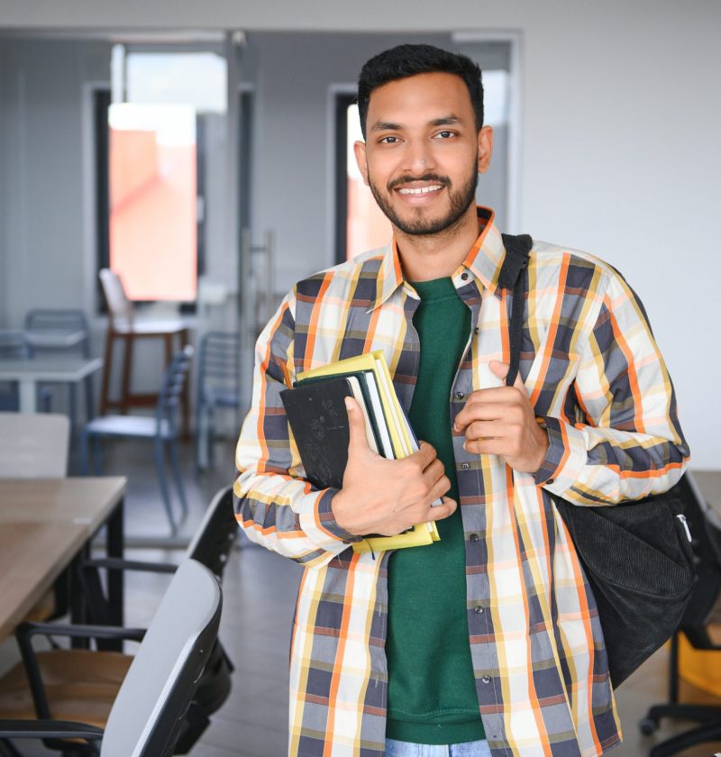 Handsome young Indian boy student with books and backpack at university. Education concept.